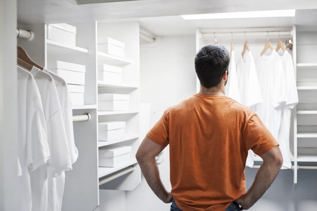 Hispanic man in a closet full of white clothes.