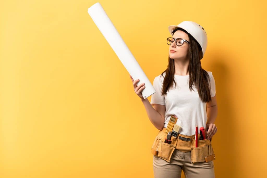 thoughtful handywoman holding and looking at blueprint on yellow background