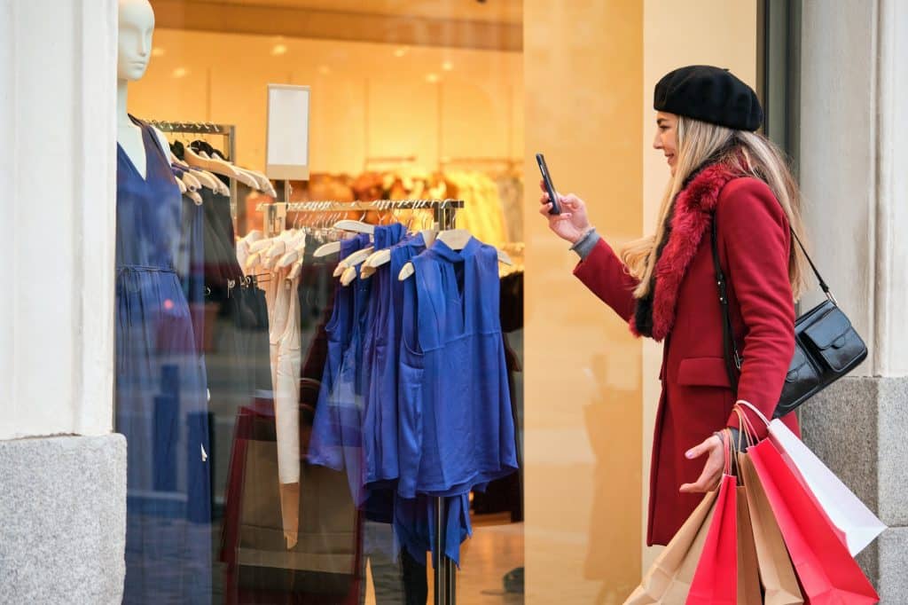 Young woman taking photos to the clothes in a store window while shopping.